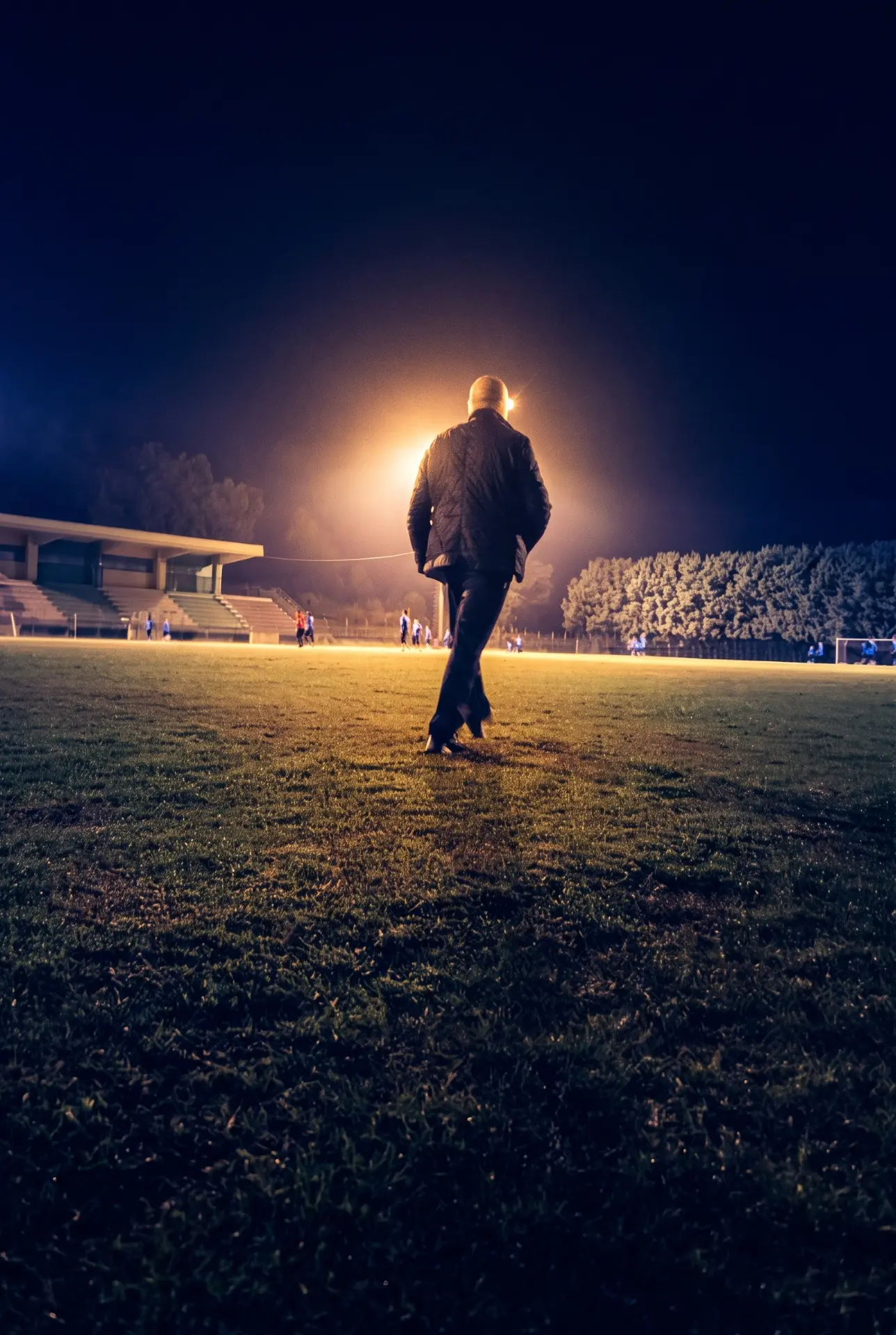 Un uomo cammina su un campo da calcio illuminato dai riflettori, di notte