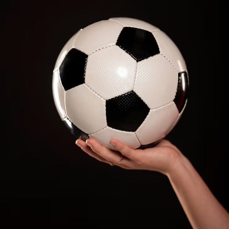 Un pallone da calcio classico bianco e nero tenuto in mano su sfondo scuro